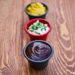 Immagine che mostra un cucchiaio di zucchero versato in una pentola di sugo rosso.